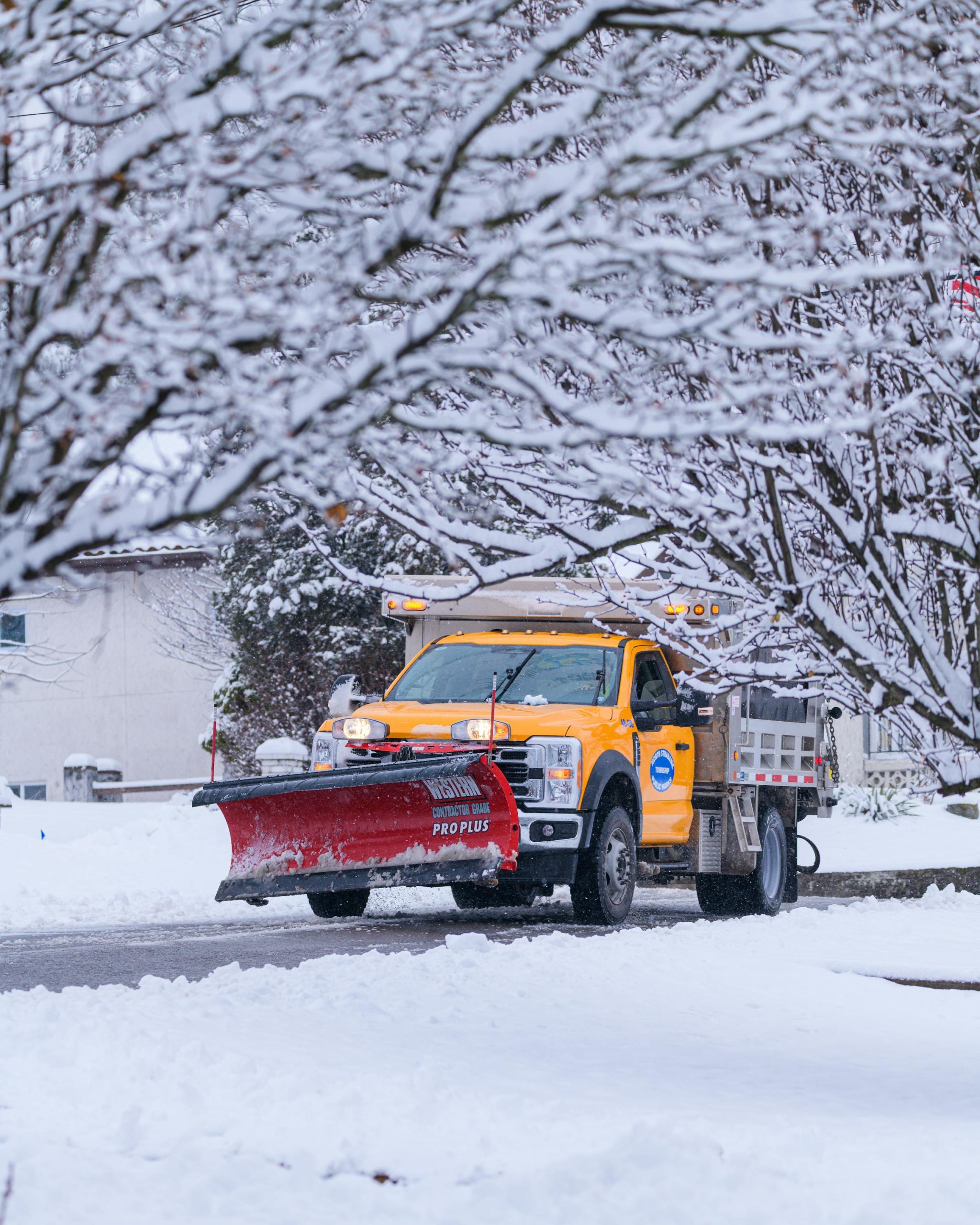 Yellow plow truck clearing a snowy residential street